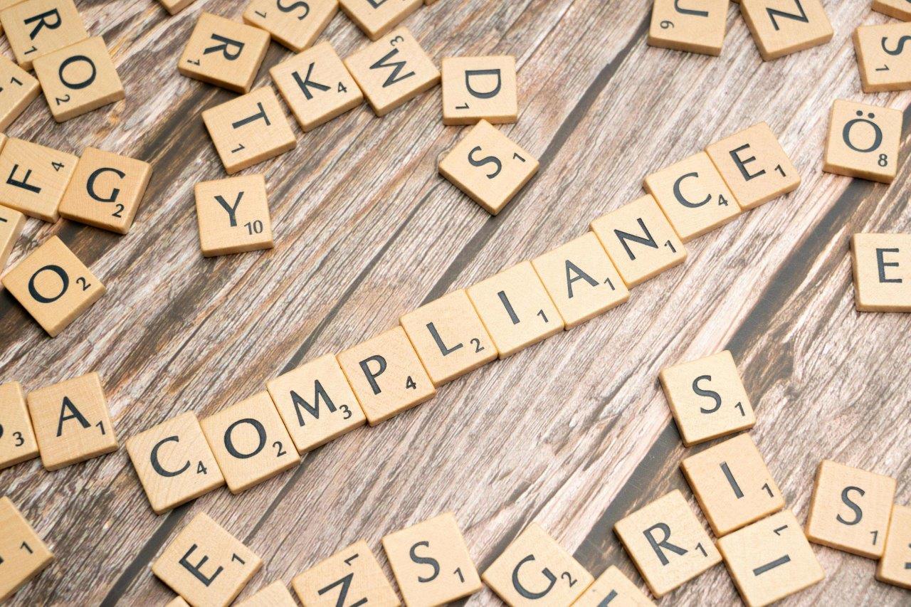 Holzbuchstaben auf einem Holztisch, die das Wort 'COMPLIANCE' bilden