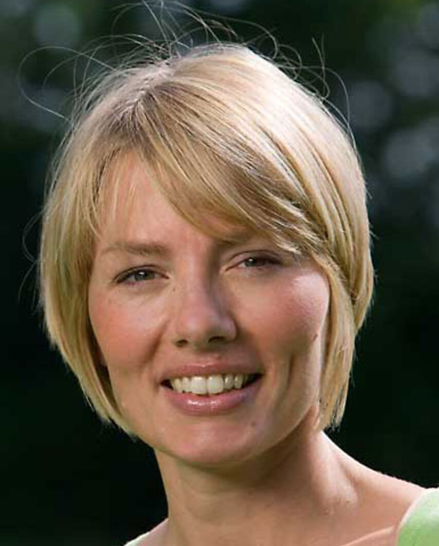 Person mit kurzen blonden Haaren, trägt grünes Oberteil, vor unscharfem dunklem Hintergrund