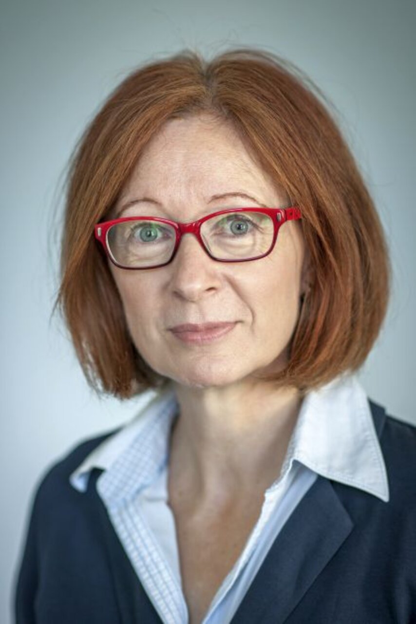 Frau mit schulterlangem, rotbraunem Haar, trägt weißen Hemdkragen und dunkelblauen Blazer