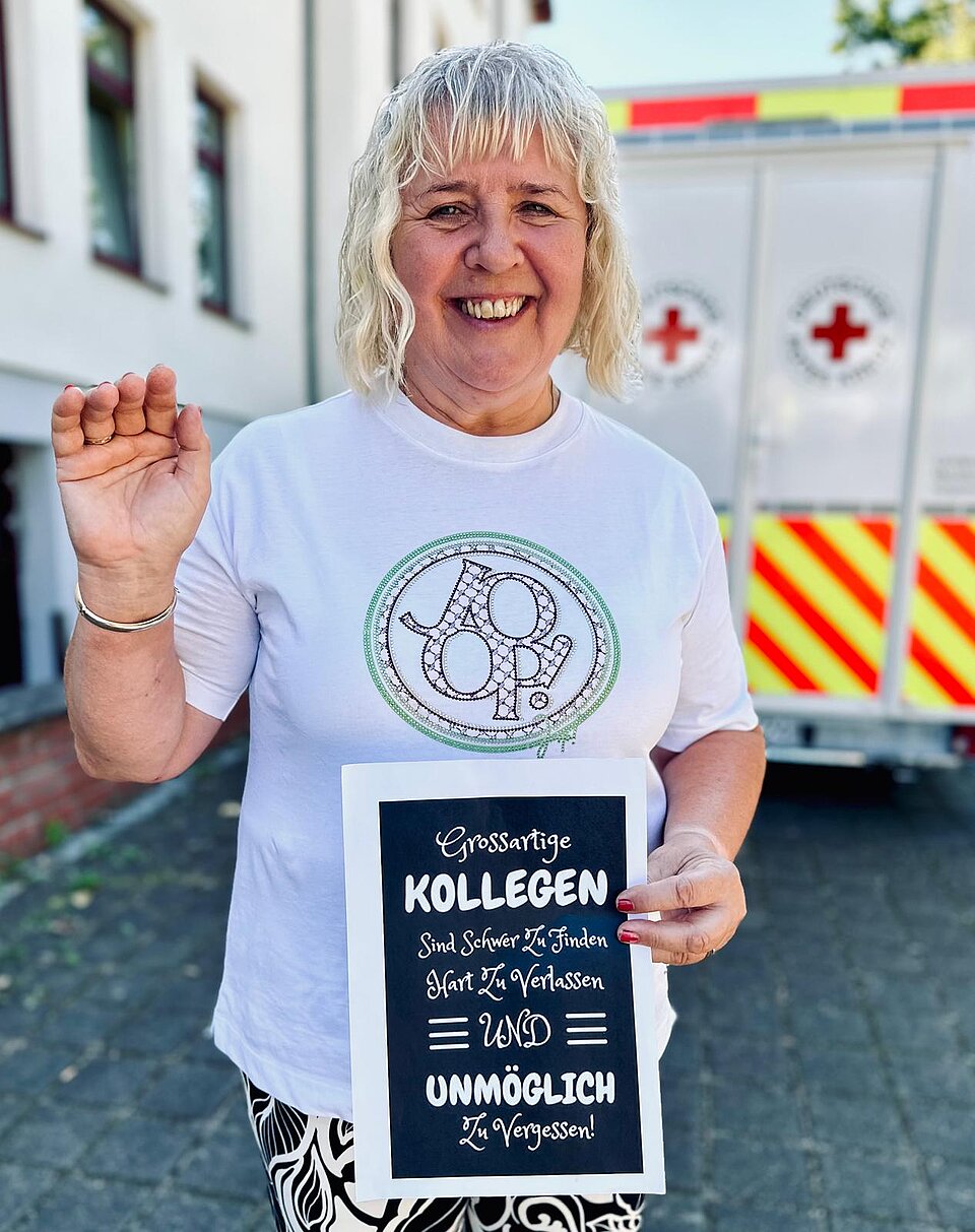 Lächelnde Person hält Schild mit Text: „Großartige Kollegen sind schwer zu finden, hart zu verlassen und unmöglich zu verg...